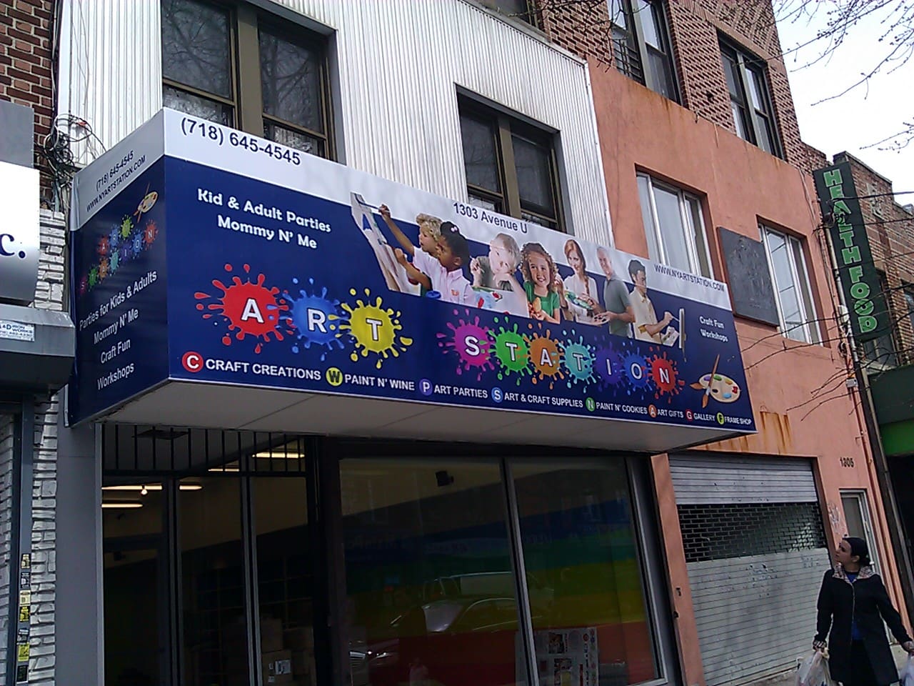 Storefront of ADP USA Solutions Gallery with colorful sign featuring images of children painting, contact number, and various service offerings listed.