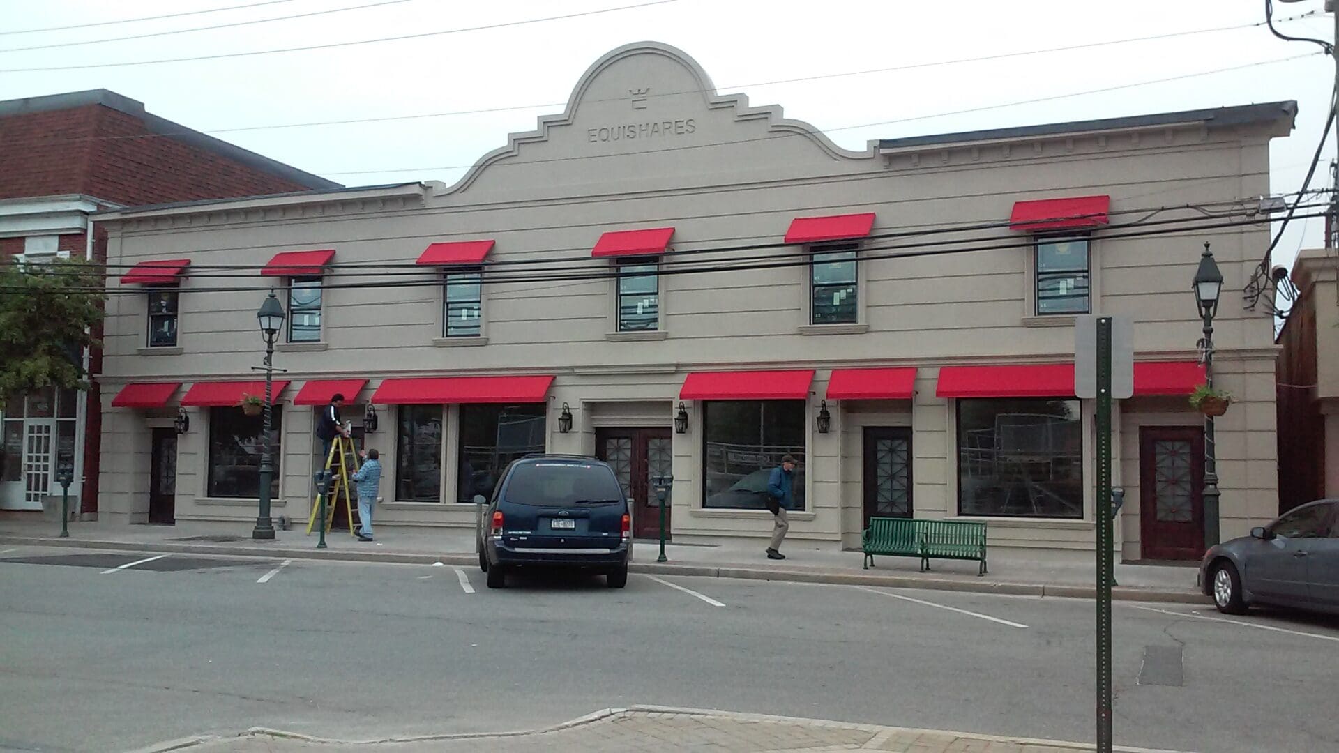 Exterior view of a beige building with red awnings, labeled 'ADP USA Solutions Gallery', featuring a man walking and another using a survey instrument by parked cars.