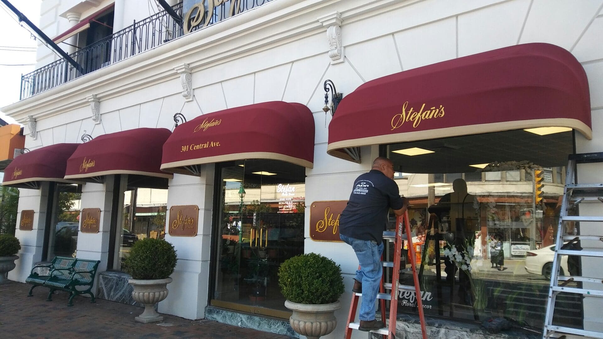 A worker on a ladder adjusts the awning of 