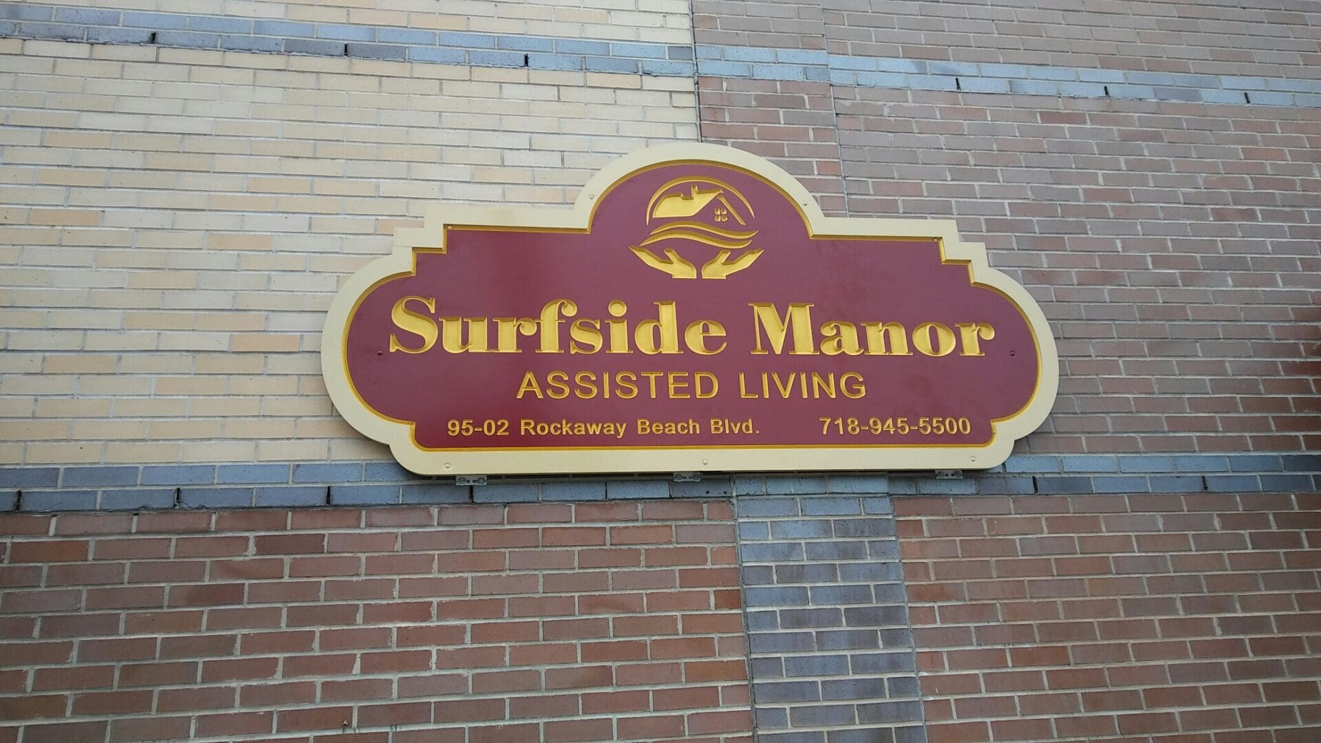 Sign for Surfside Manor Assisted Living with ADP USA Solutions Gallery and phone number on a brick wall.