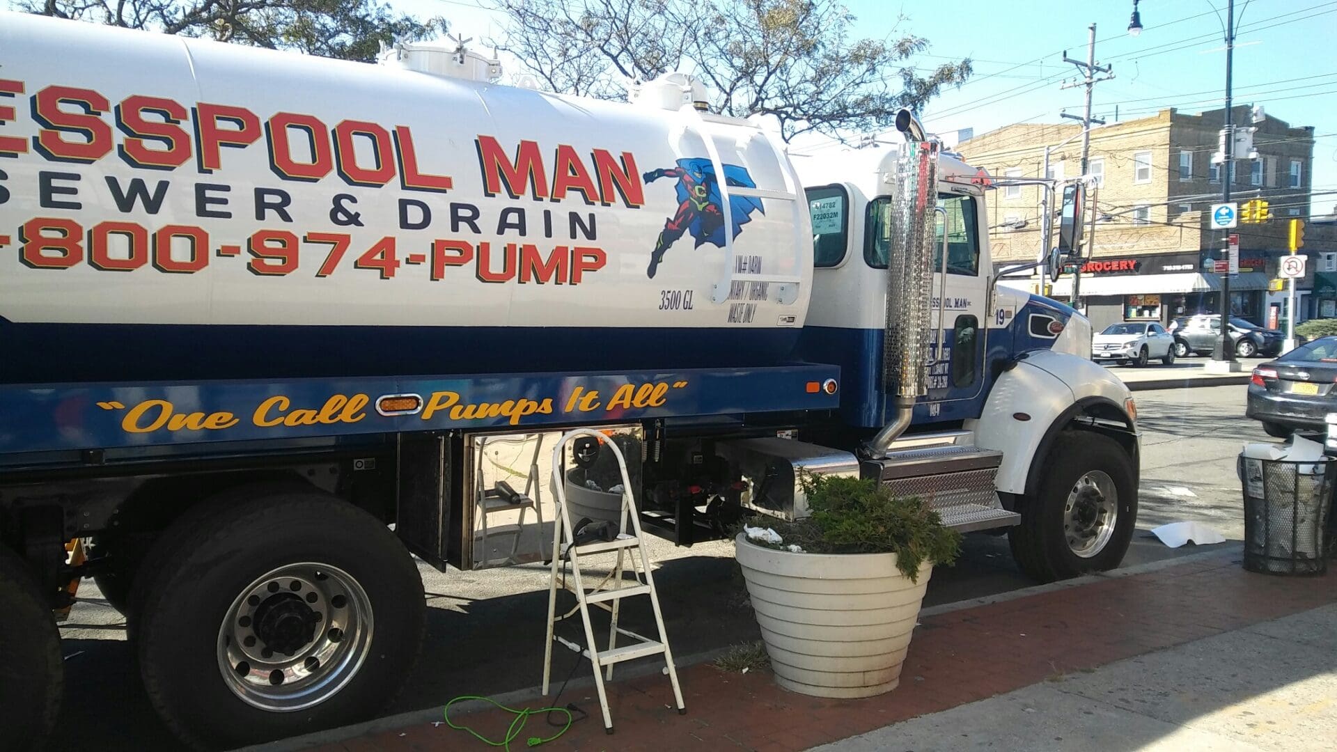 A large sewer and drain service truck parked on a sunny street, featuring bold text and a graphic of a superhero plumber from ADP USA Solutions Gallery.