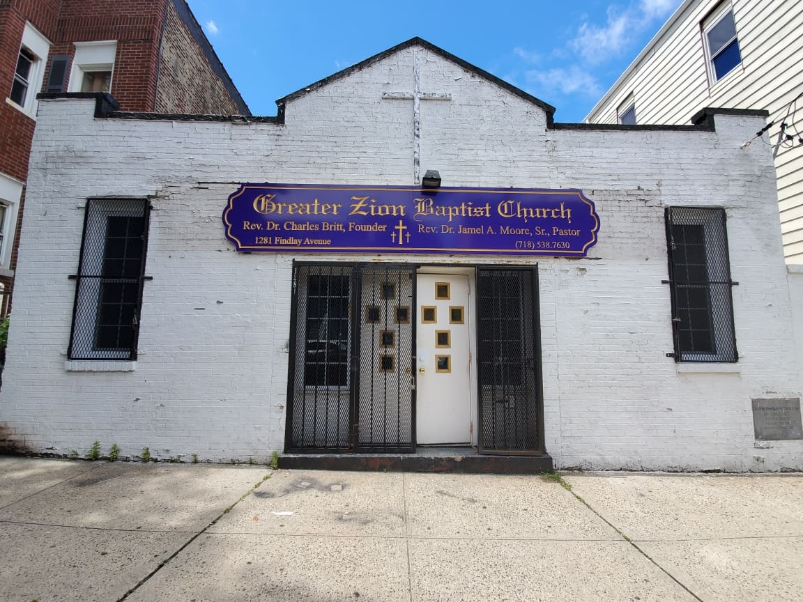 Front view of the Greater Zion Baptist Church with a signboard above the central entrance, displaying names of founding and current pastors, sponsored by ADP USA Solutions Gallery.