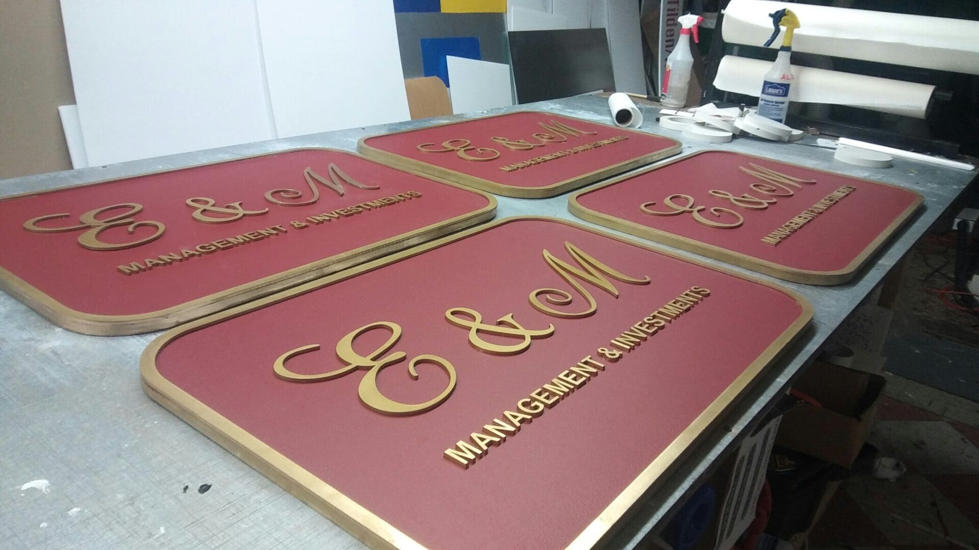 Four custom-made signs on a workshop table, each featuring the logo 
