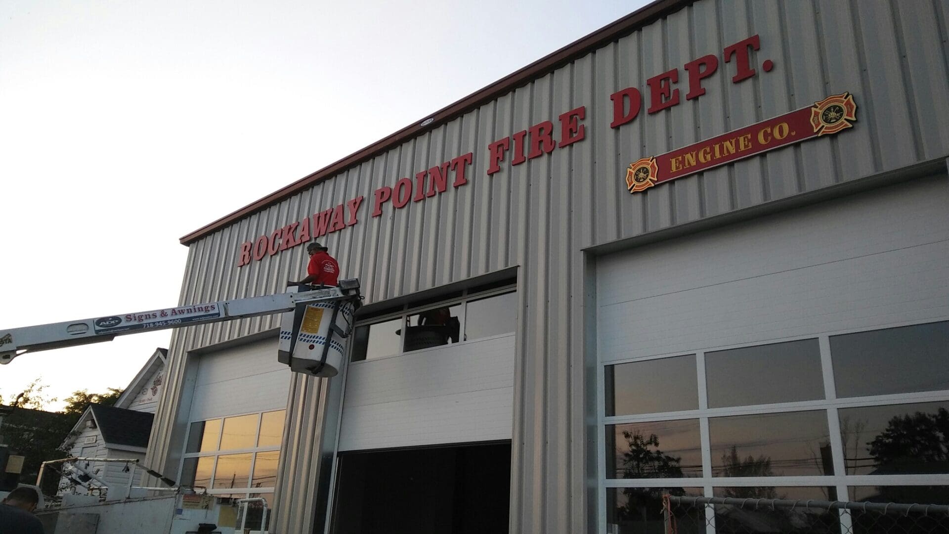 Firefighters on a lift installing a sign on the ADP USA Solutions Gallery building at dusk.