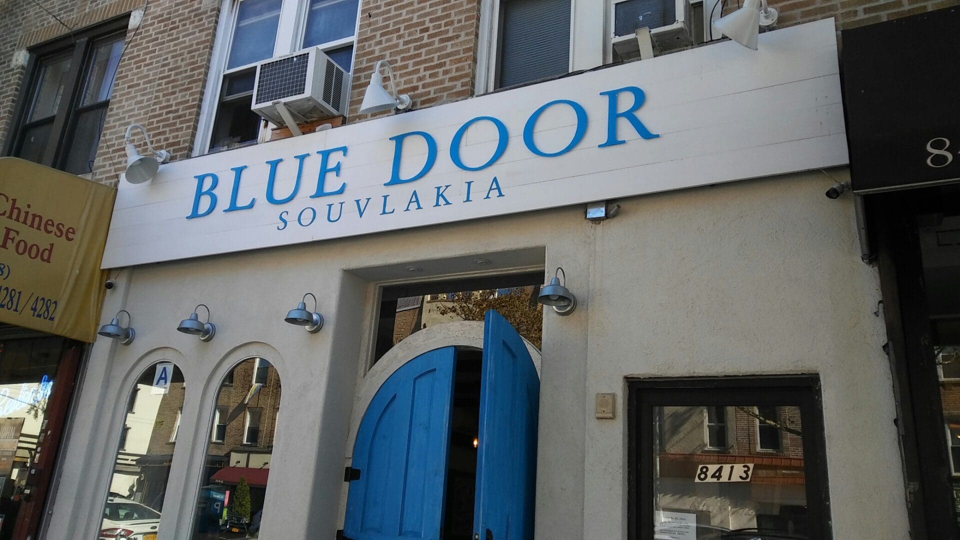 Front view of blue door souvlaki restaurant, featuring a brick facade with a bold sign above a bright blue door, flanked by arched windows in the ADP USA Solutions Gallery.
