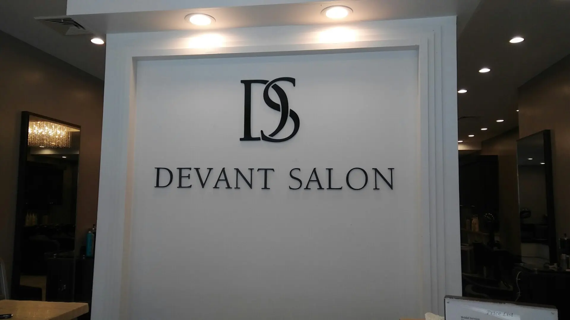 Signage of deviant salon with a logo above the text, displayed on a gray wall inside a well-lit gallery.