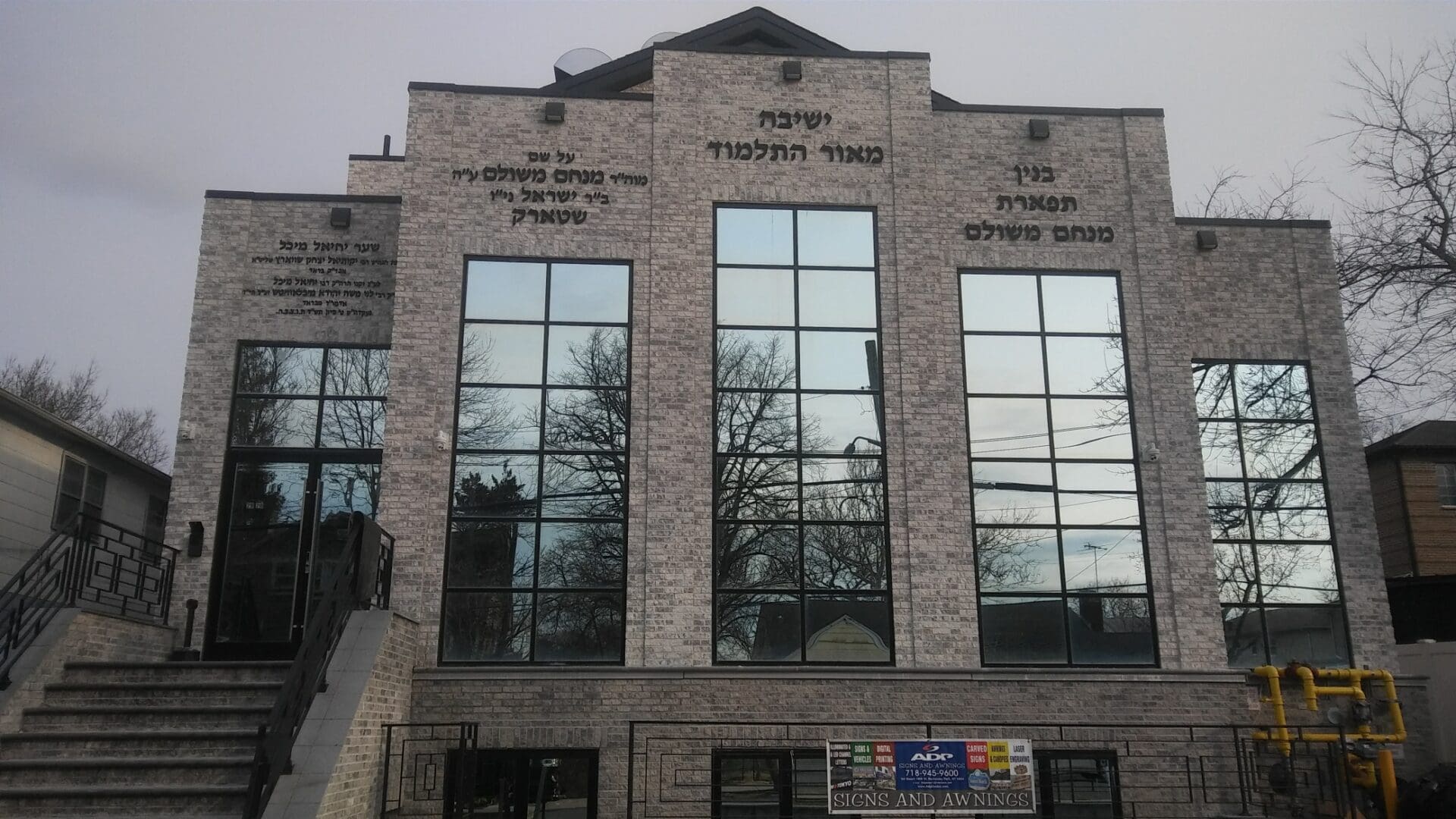 Exterior of a modern stone building with large windows, featuring Hebrew inscriptions and architectural symmetry, part of the ADP USA Solutions Gallery.