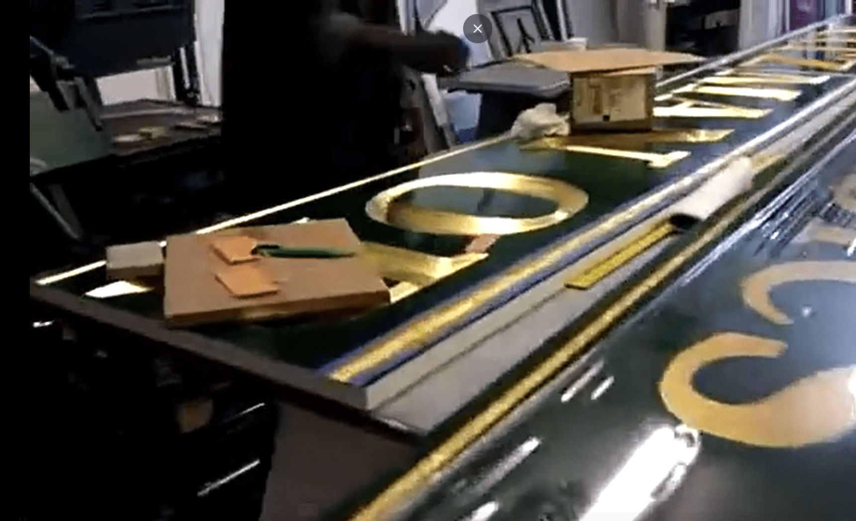 A worker oversees a production line with gold numbers being applied to a green surface in the ADP USA Solutions Gallery.