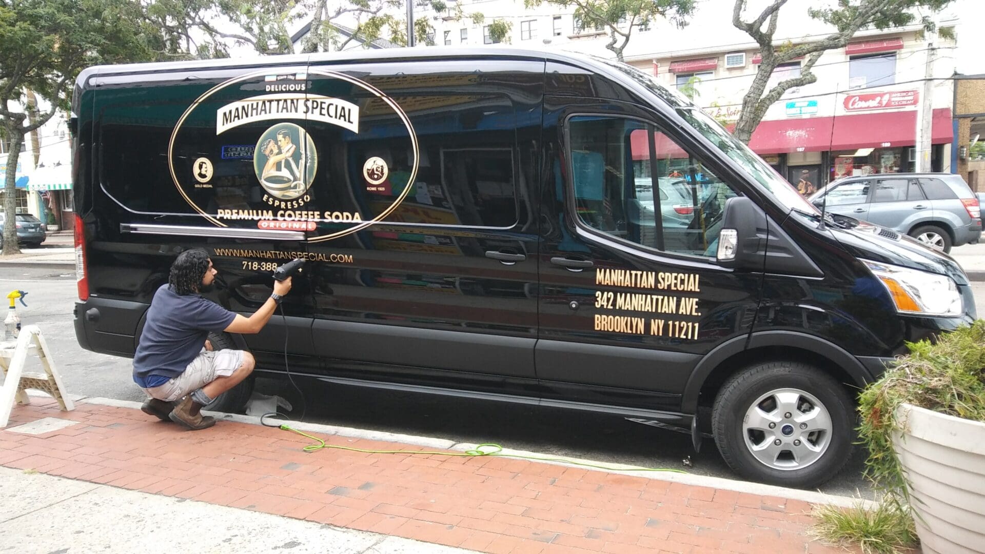 A man applies an advertisement decal for ADP USA Solutions Gallery to a black van parked on a city street.