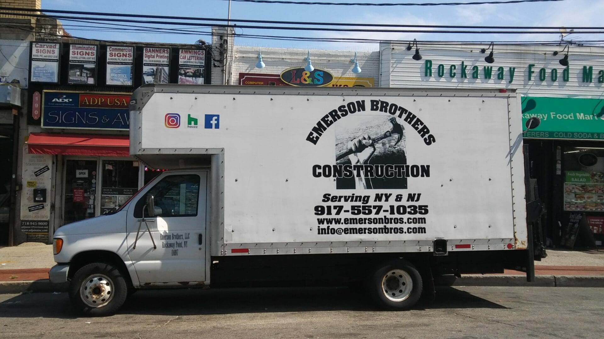 A white ADP USA Solutions Gallery truck parked on a street, with business contact details and logo on its side, in front of a row of small shops.