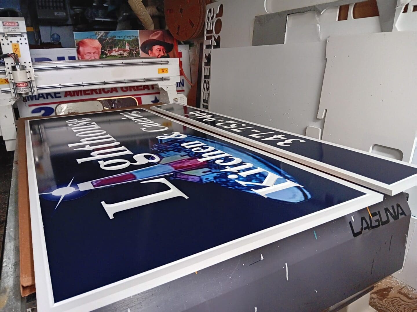 Large format printer producing a blue and white advertising banner for ADP USA Solutions Gallery with inverted text, inside a cluttered workshop with various tools and materials visible.